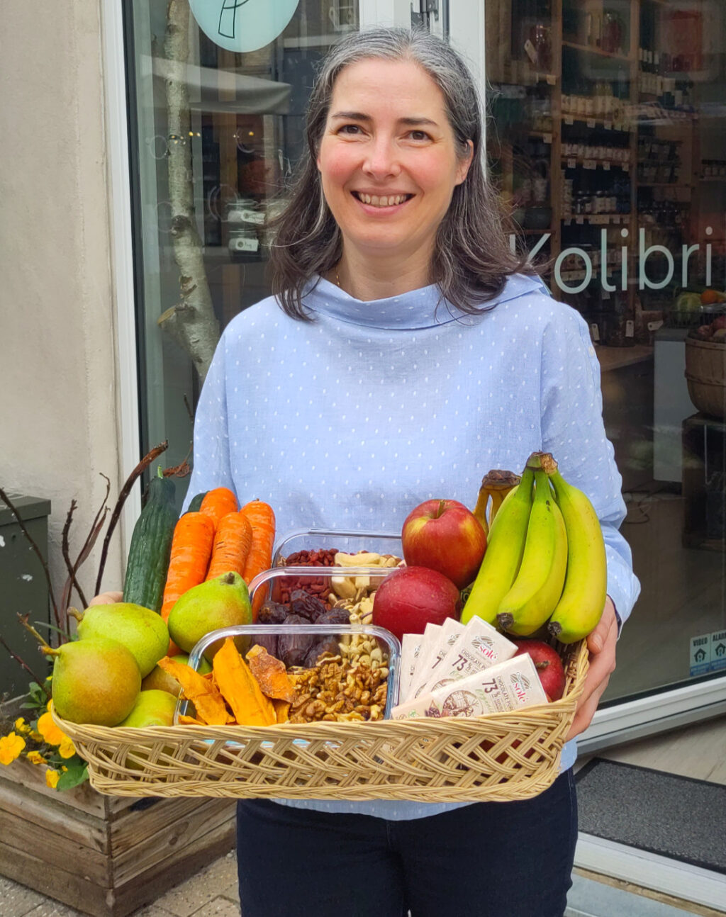 Véronique med en kurv med økologisk firmafrugt og snacks, gnavegrønt og mørk chokolade.